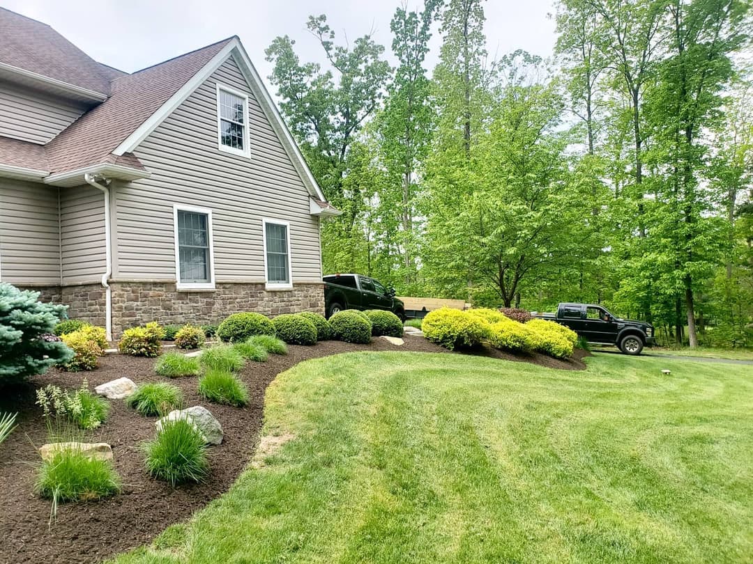 Beautiful landscaped home exterior with manicured garden near lush greenery and parked trucks.