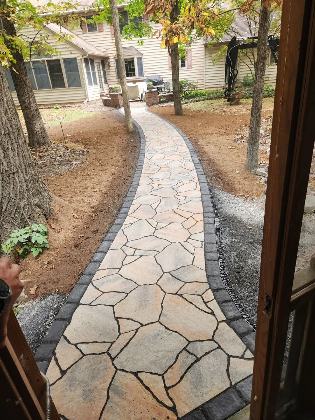 Stone pathway leading through trees to a backyard with landscaped area and home.