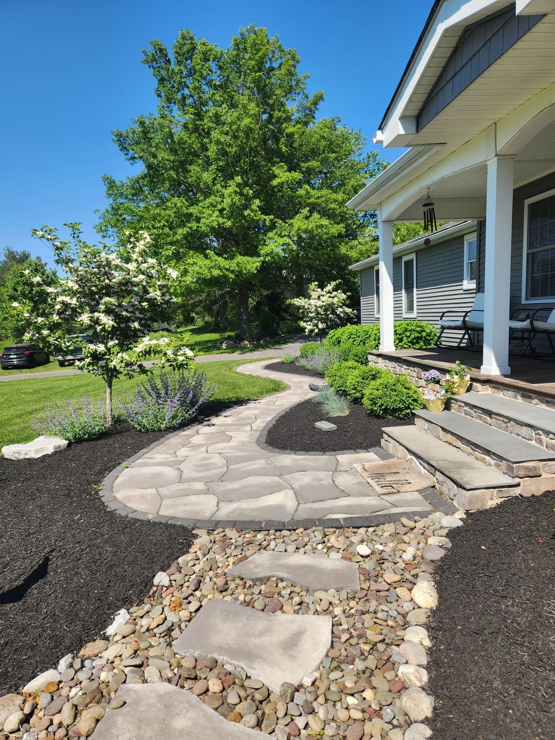 Pathway with stone and gravel borders leading to a house with landscaped gardens and greenery.