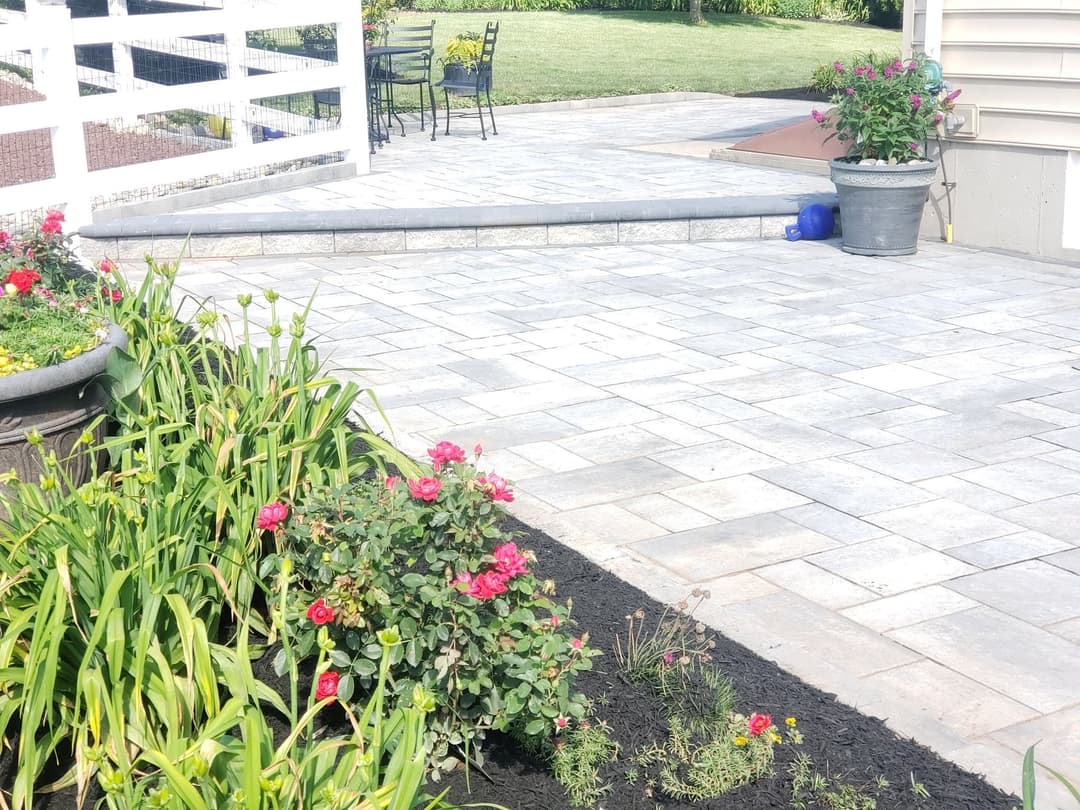Patio with stone pavers, vibrant flowers, and outdoor seating area in a landscaped garden.