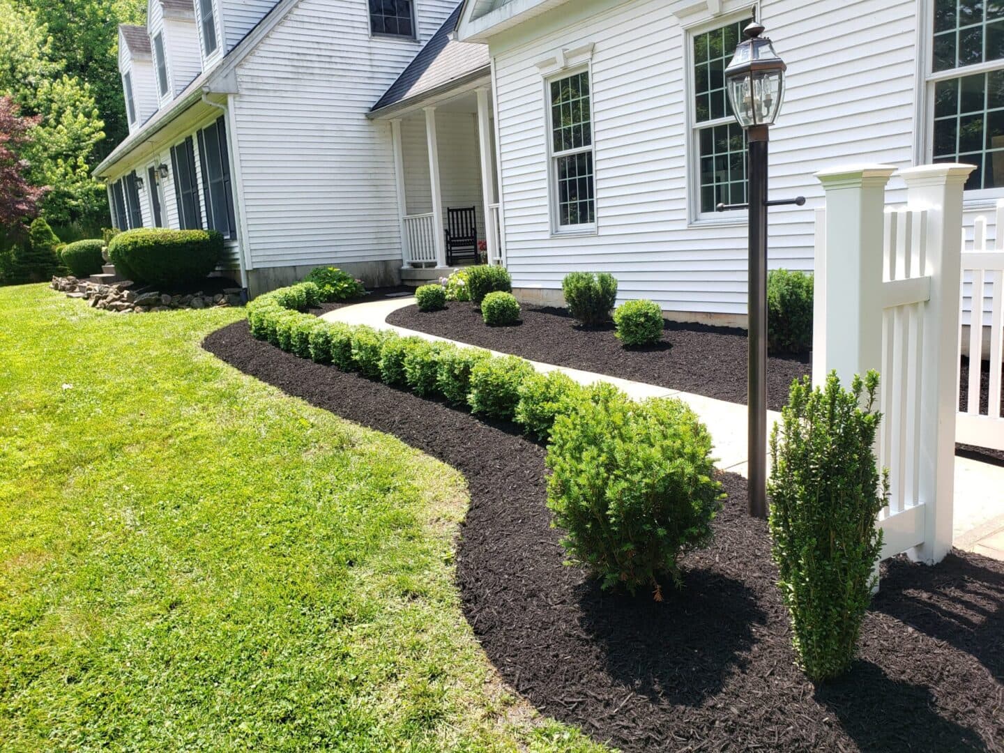 Lush landscaping with trimmed bushes and mulch path beside a white house on a sunny day.