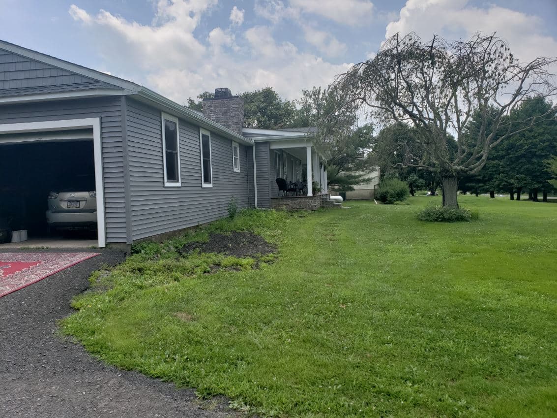 Gray house with porch, green lawn, and tree, surrounded by a peaceful outdoor setting.