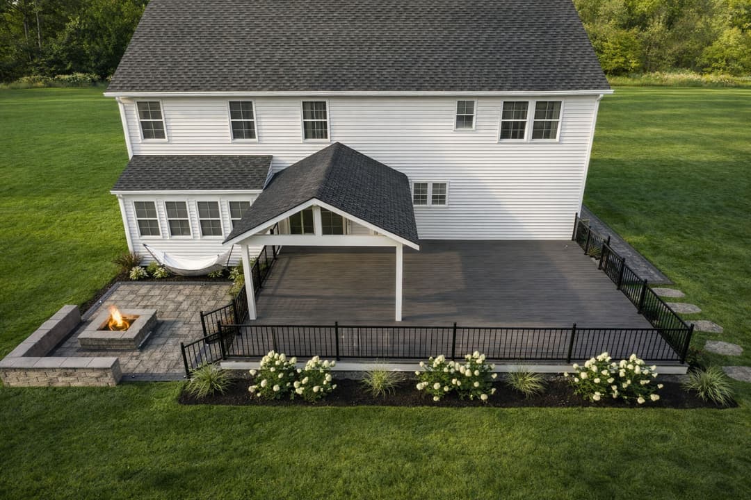 Aerial view of a modern house with a spacious deck, firepit, and landscaped yard.