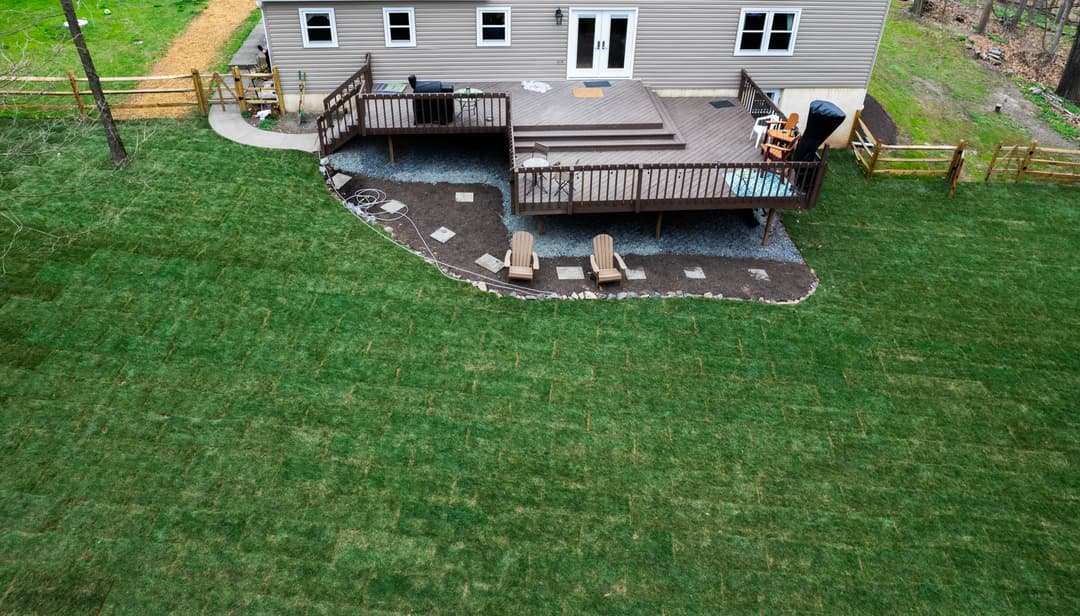 Cleared land near a house with a tractor and scattered trees under a blue sky.