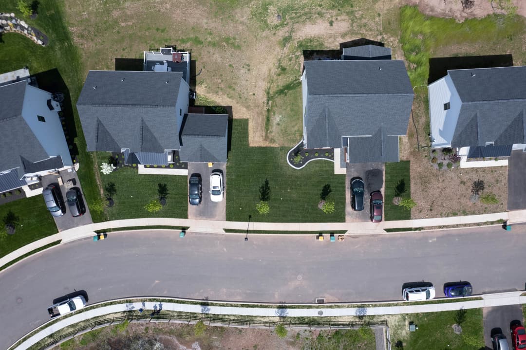 Aerial view of residential neighborhood showcasing houses, lawns, and parked cars.