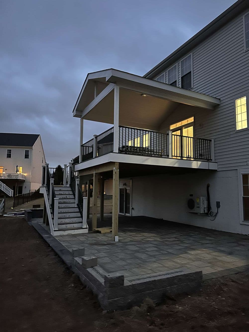 Newly built home exterior with a covered deck, stairs, and illuminated windows at dusk.