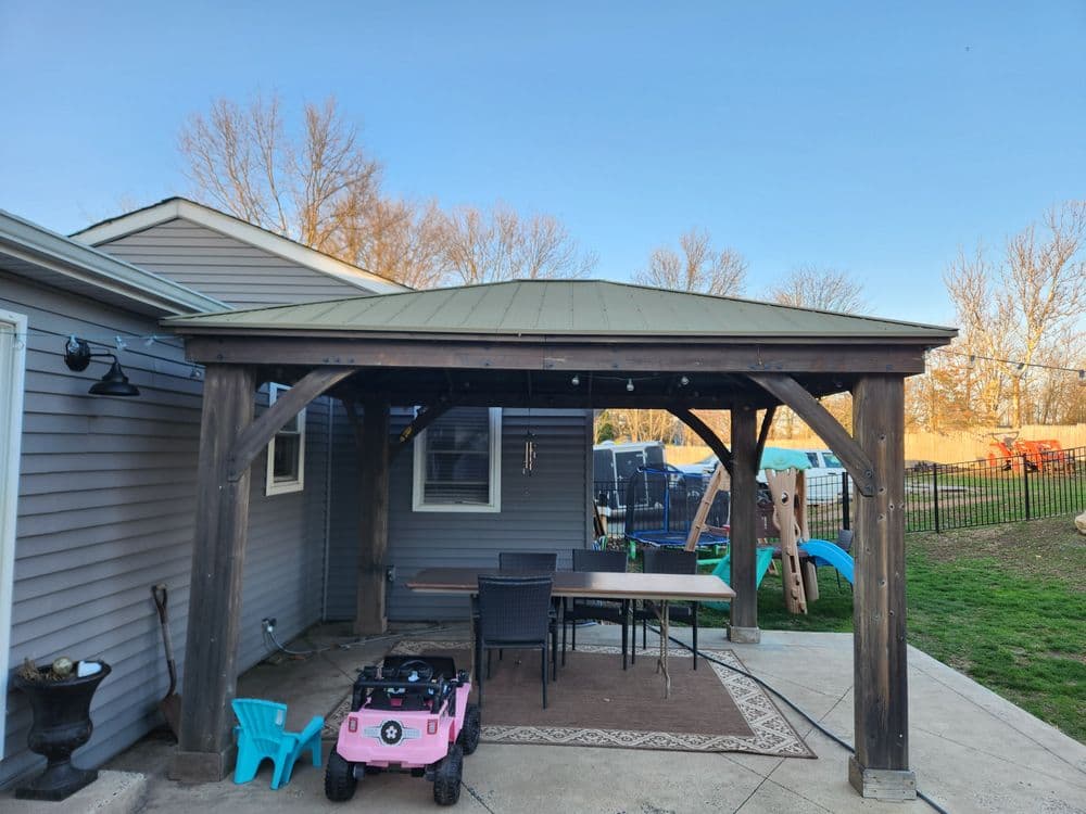 Outdoor patio with a wooden gazebo, dining table, and children's toys in the background.