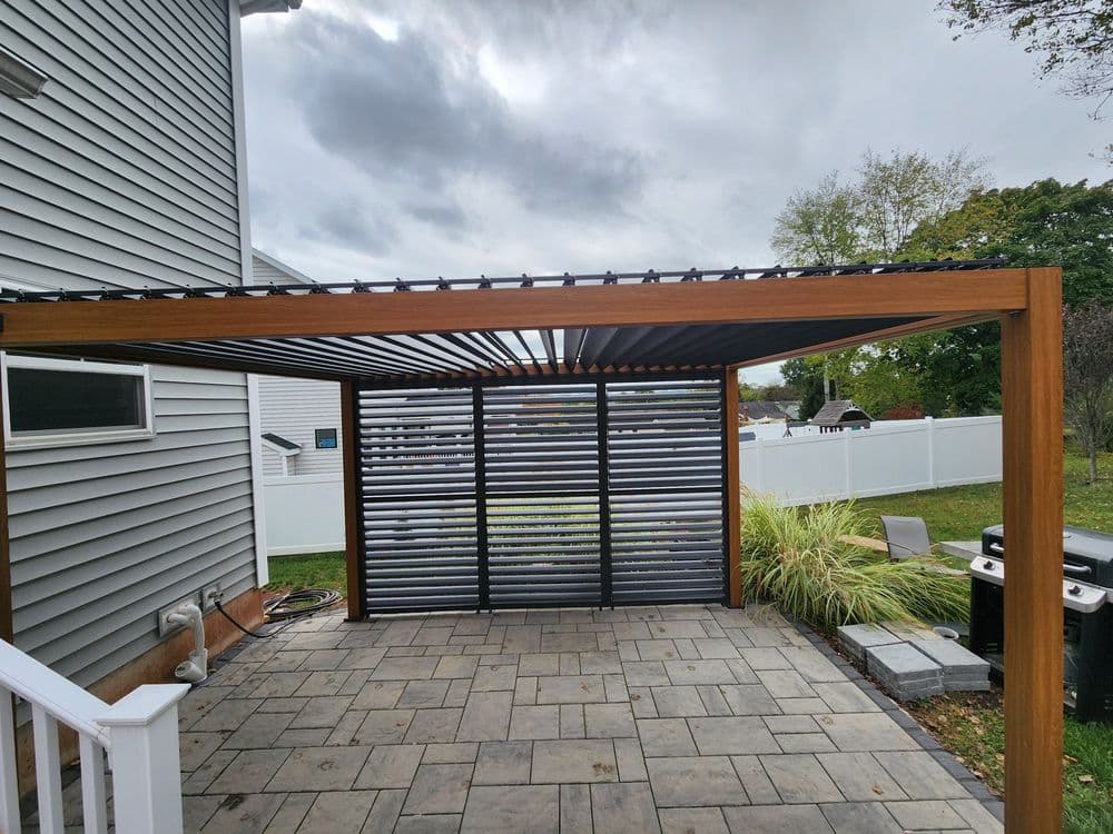 Modern wood pergola with adjustable slats in a backyard patio setting. Gray sky in background.