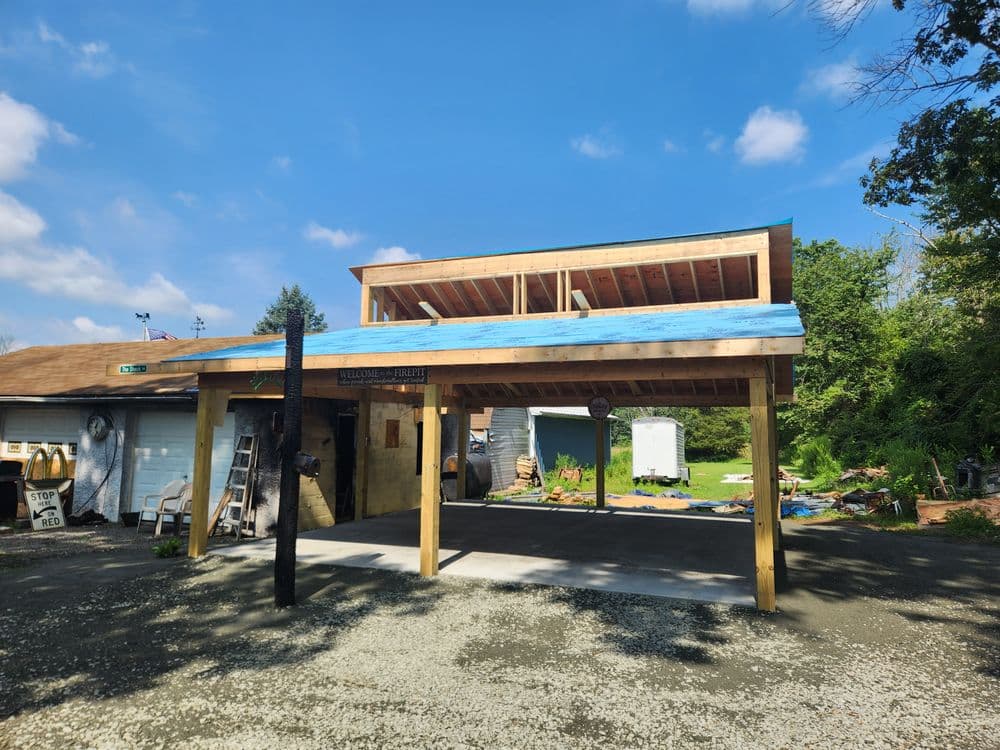 Newly constructed carport with a blue roof against a clear sky and surrounding greenery.