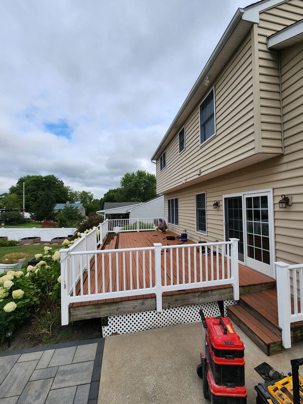 Spacious wooden deck with white railing, adjacent to a home and landscaped garden.
