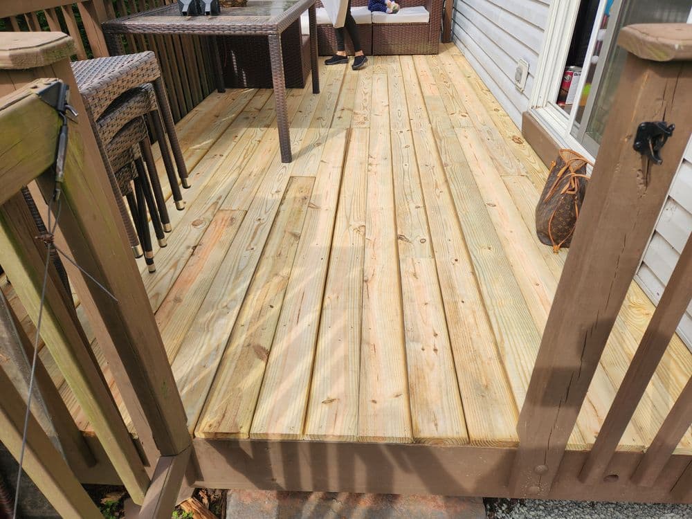 Newly installed wooden deck with outdoor furniture and sunlight casting shadows.