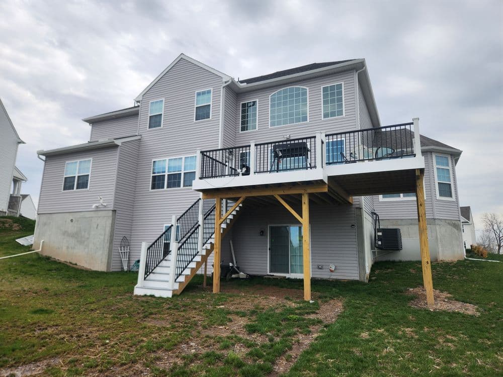 Two-story gray house with a deck and patio in a suburban setting, featuring a grassy lawn.