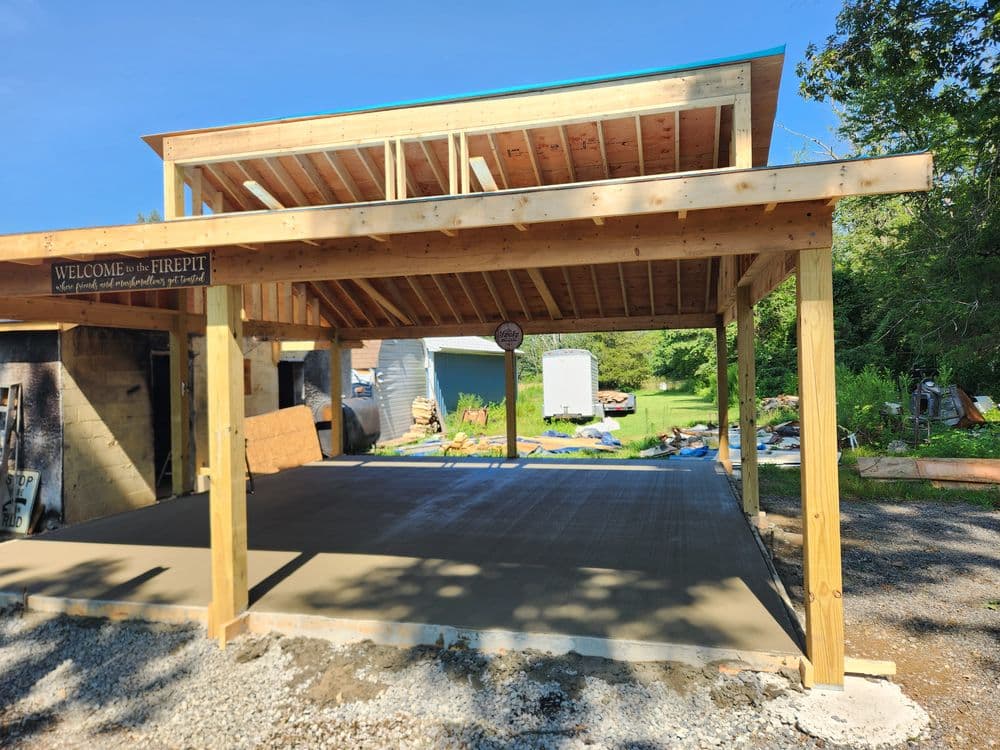 Newly constructed shelter featuring a concrete floor, open structure, and sign for a firepit area.