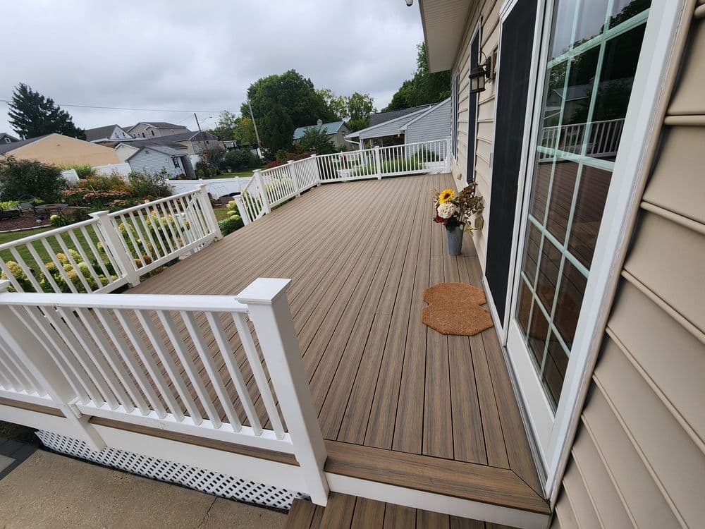 Newly renovated wooden deck with white railings and decorative flowers, surrounded by gardens.