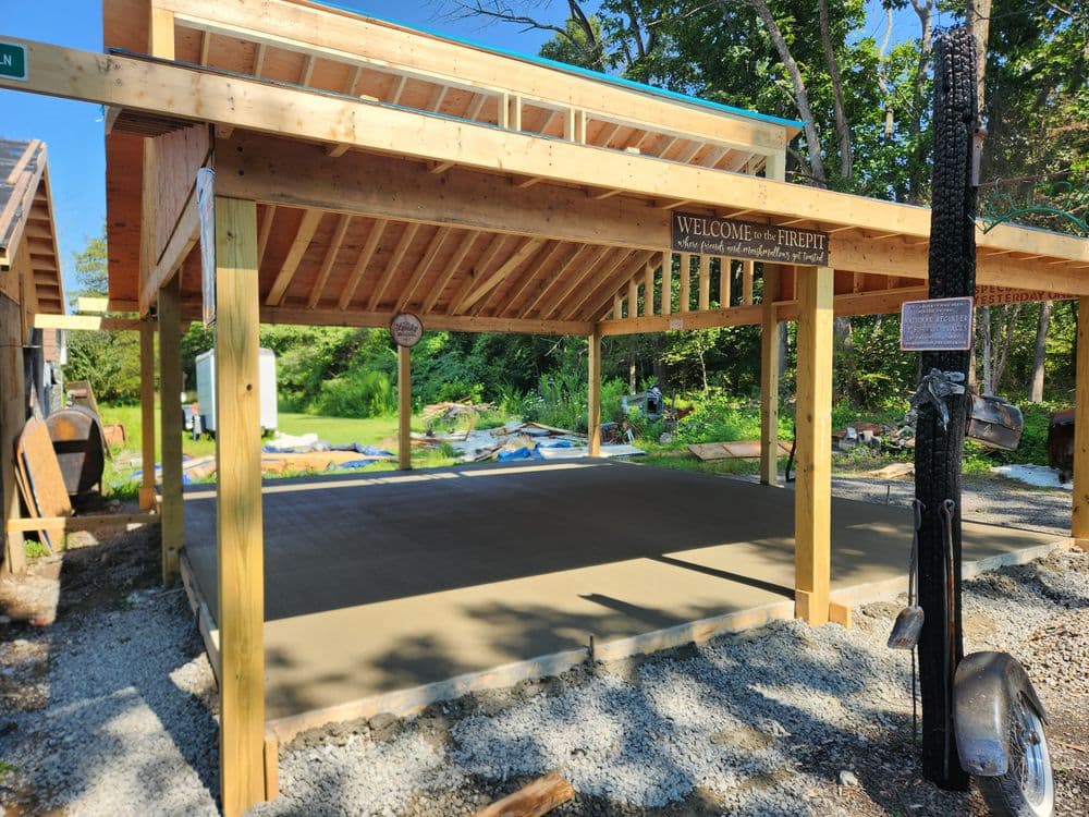Open air pavilion with wooden structure and sign welcoming visitors, surrounded by greenery.