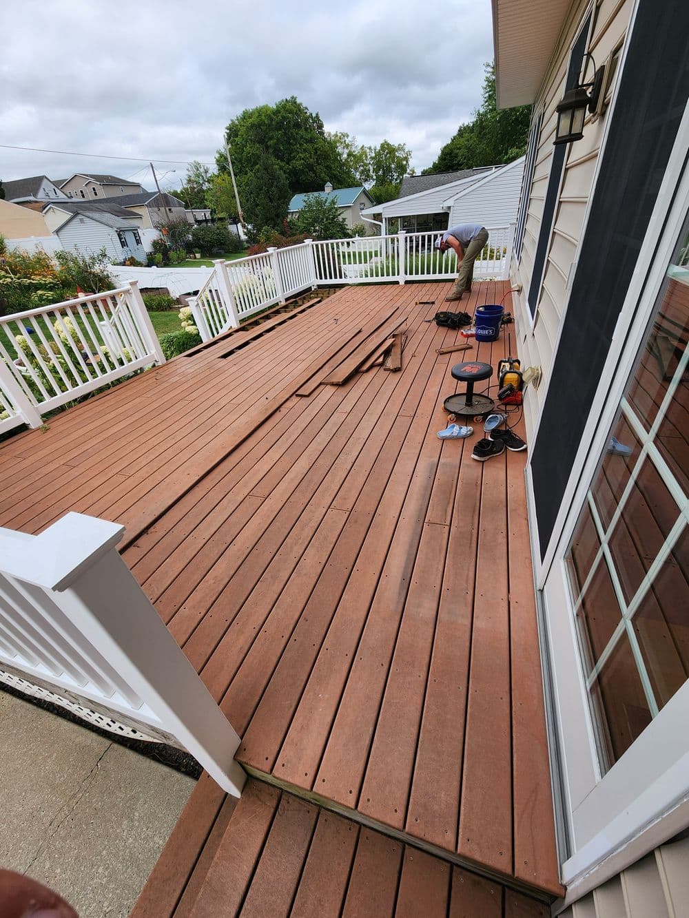 Person installing new wooden decking on a residential porch with tools nearby.