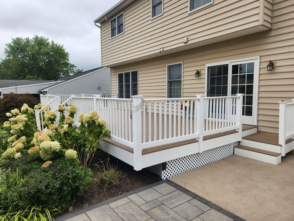 Modern backyard deck with white railing, surrounded by lush green landscaping and flowers.