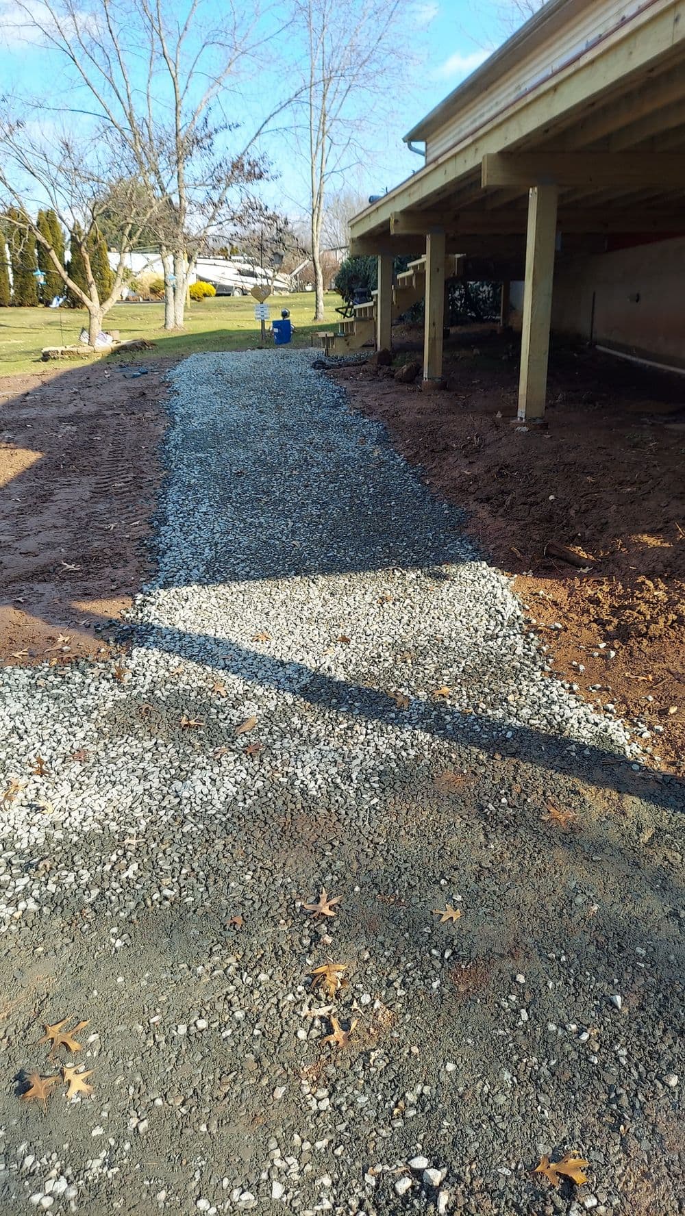 Gravel pathway under a porch with clear blue sky and trees in the background.