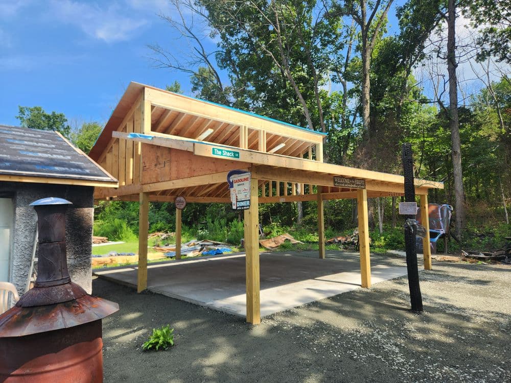 Newly built open-air pavilion under construction in a wooded area with concrete flooring.