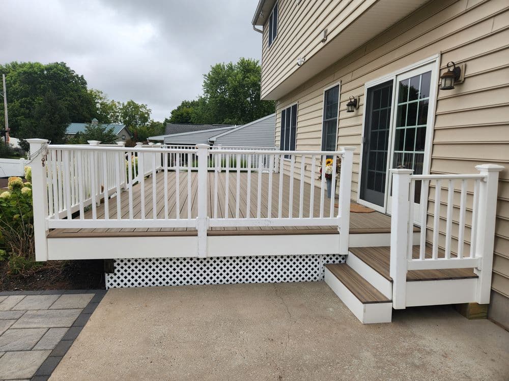 Modern wooden deck with white railings and steps beside a beige house on a cloudy day.