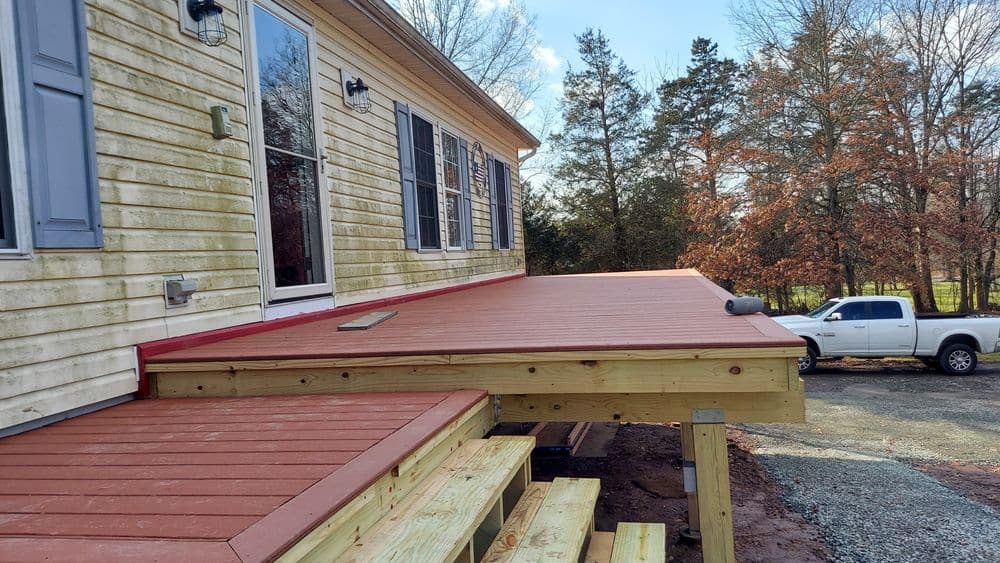Newly constructed outdoor deck with red finish, adjacent to a house and parked truck.