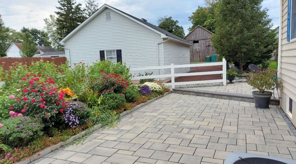 Lush garden with colorful flowers and paved pathway by a house and fence.