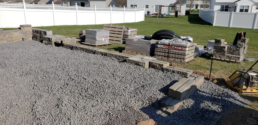 Construction site with gravel, stone blocks, and pallets in a residential yard.