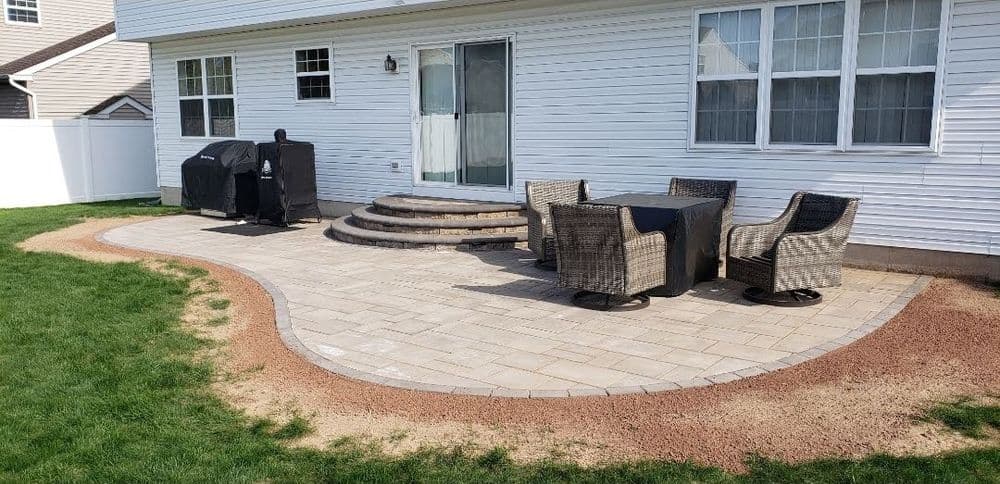 Backyard patio with paver stones, outdoor seating, grill, and grass area.