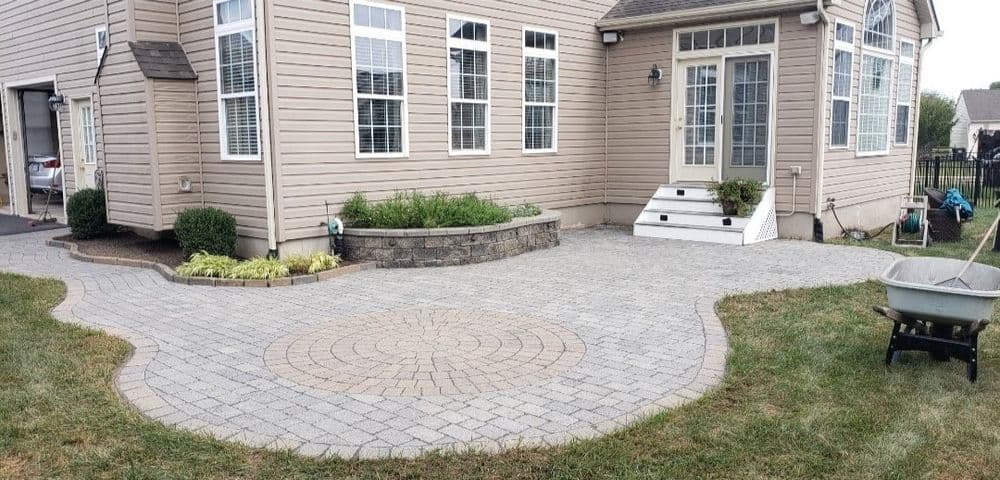 Paved patio with circular pattern, stone flower bed, and side entrance to home.