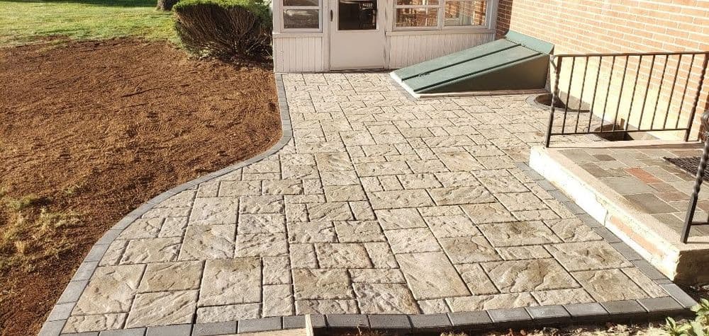 Paved stone patio leading to a house with landscaped yard and stairs.