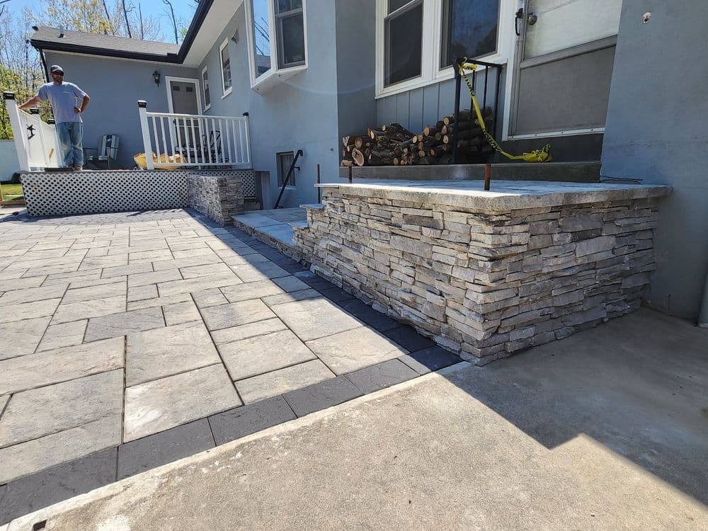 Newly paved patio with stone wall and steps, featuring a person in the background.