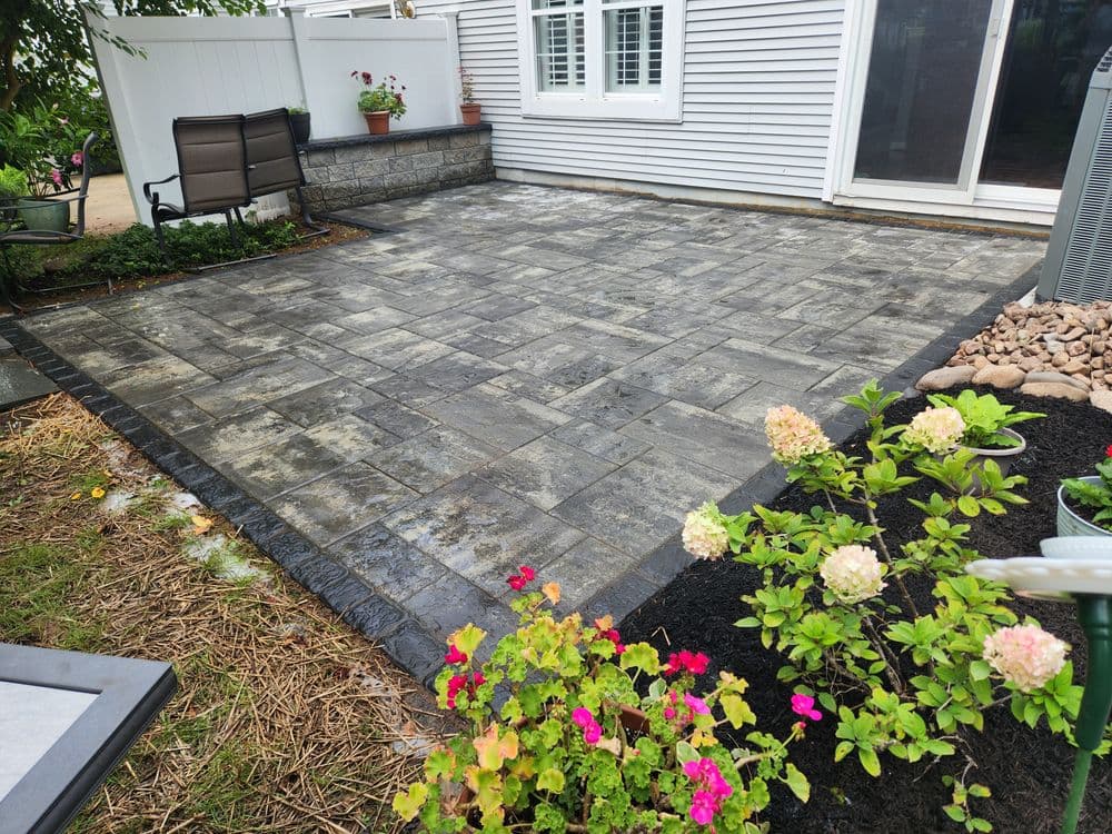 Patio with gray pavers, surrounded by flowers and landscaping, ideal for outdoor relaxation.
