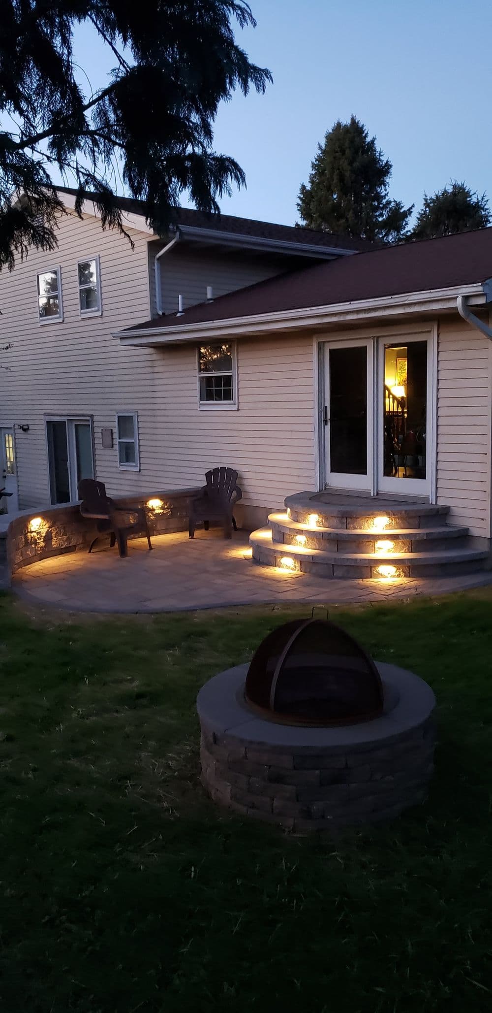 Cozy outdoor patio with steps, lighting, and seating near a house at dusk.