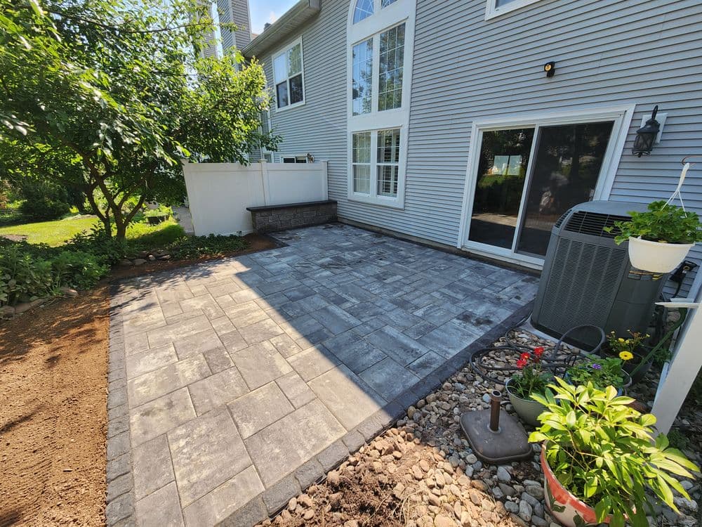Patio area with pavers, greenery, and central air conditioning unit by a spacious home.