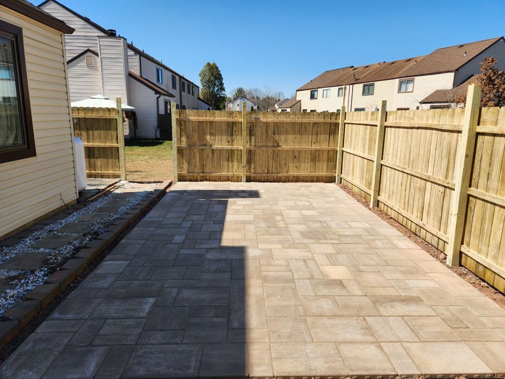 Paved backyard patio with wooden fence and clear blue sky, ideal for outdoor gatherings.