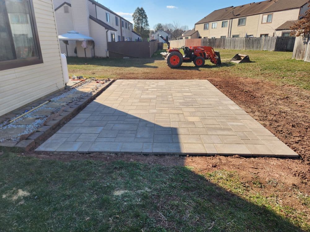Paved outdoor patio area with tractor and house in background, showcasing landscaping project.