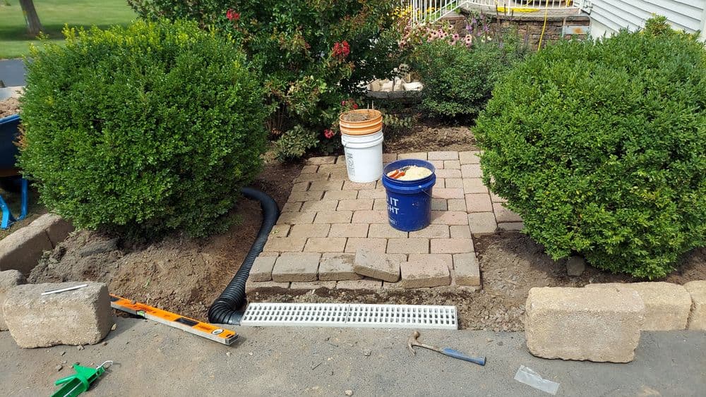 Landscaping project with boxwood shrubs, paver stones, and construction materials in garden area.