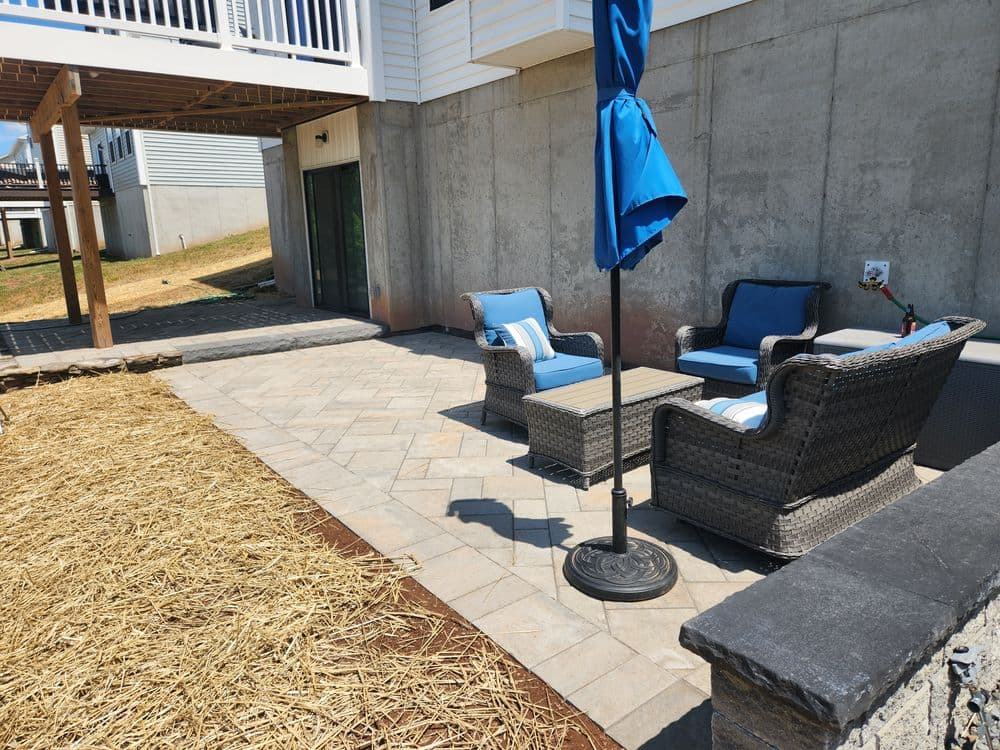 Cozy outdoor patio with wicker furniture, a blue umbrella, and a stone paver surface.