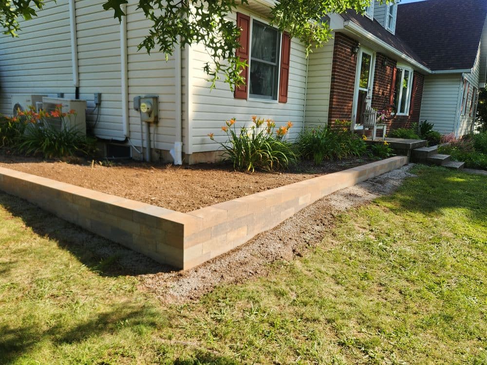 Newly constructed patio with stone edging and flower bed, surrounded by green lawn.