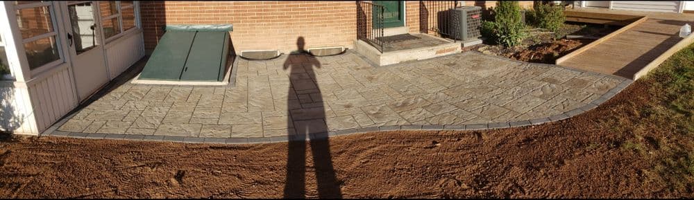 Patterned stone patio installation with a shadow in front of a brick home.