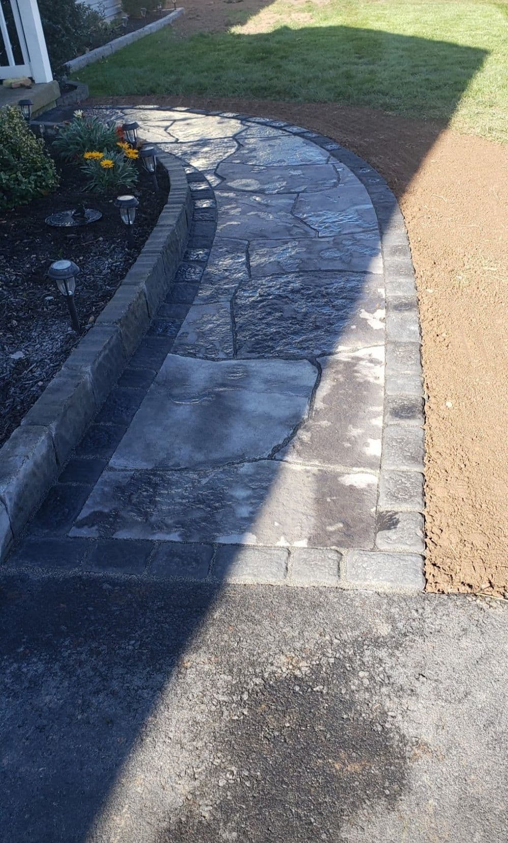 Curved stone pathway leading to a grassy area, featuring decorative lights along the edge.