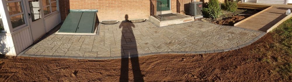 Paved patio area with stone design, shadow of a person, and upcoming landscaping.