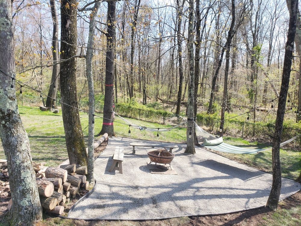 Quiet outdoor campsite with a hammock, fire pit, and picnic table surrounded by trees.