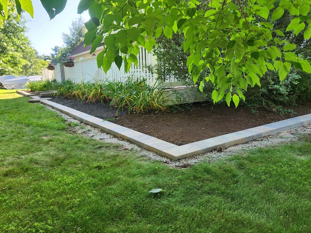 Garden landscape with freshly prepared soil, bordered by stone edging and lush greenery.