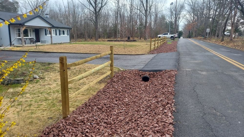 Residential driveway with gravel landscaping and wooden fences alongside a quiet road.