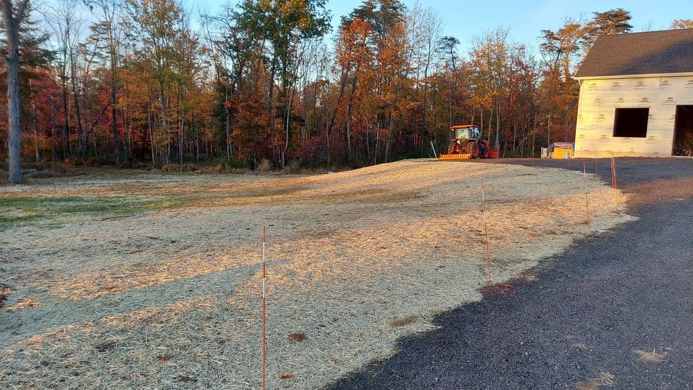 Tractor on a freshly mowed field with autumn trees and a construction site in the background.