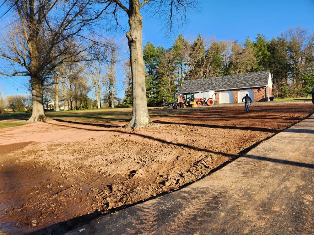Landscaping project in progress near a garage with freshly graded soil and trees.