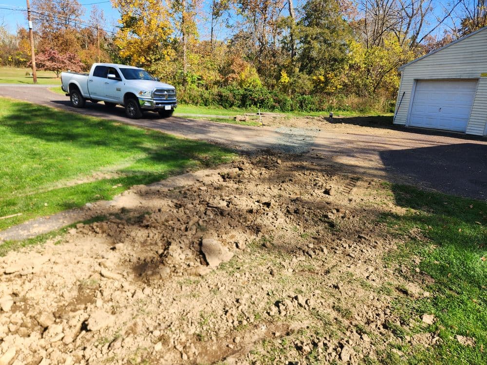Pickup truck parked near a freshly dug dirt area beside a residential garage in autumn.