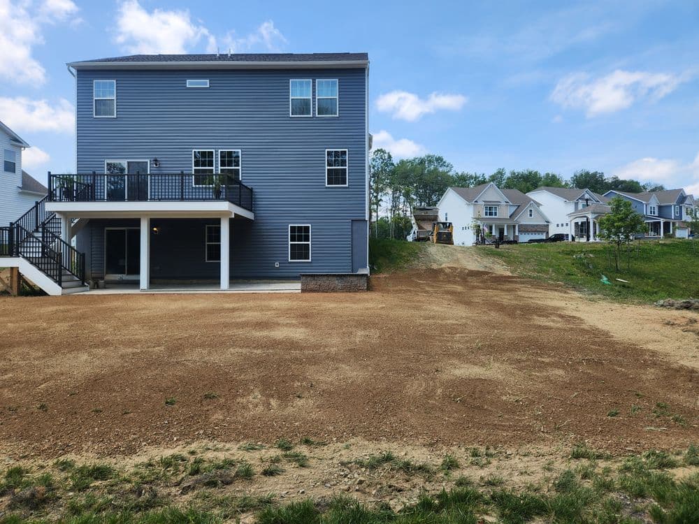 Newly constructed blue house with a yard, surrounded by other homes and clear sky.