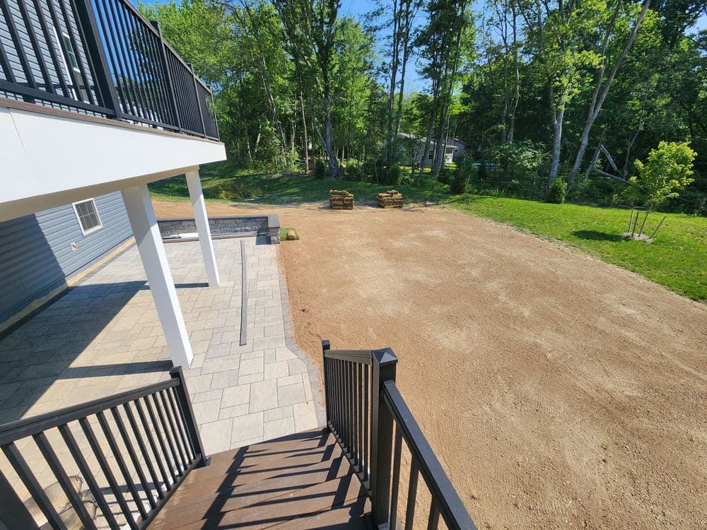 Backyard view with stone patio, stairs, and cleared area for landscaping and outdoor activities.